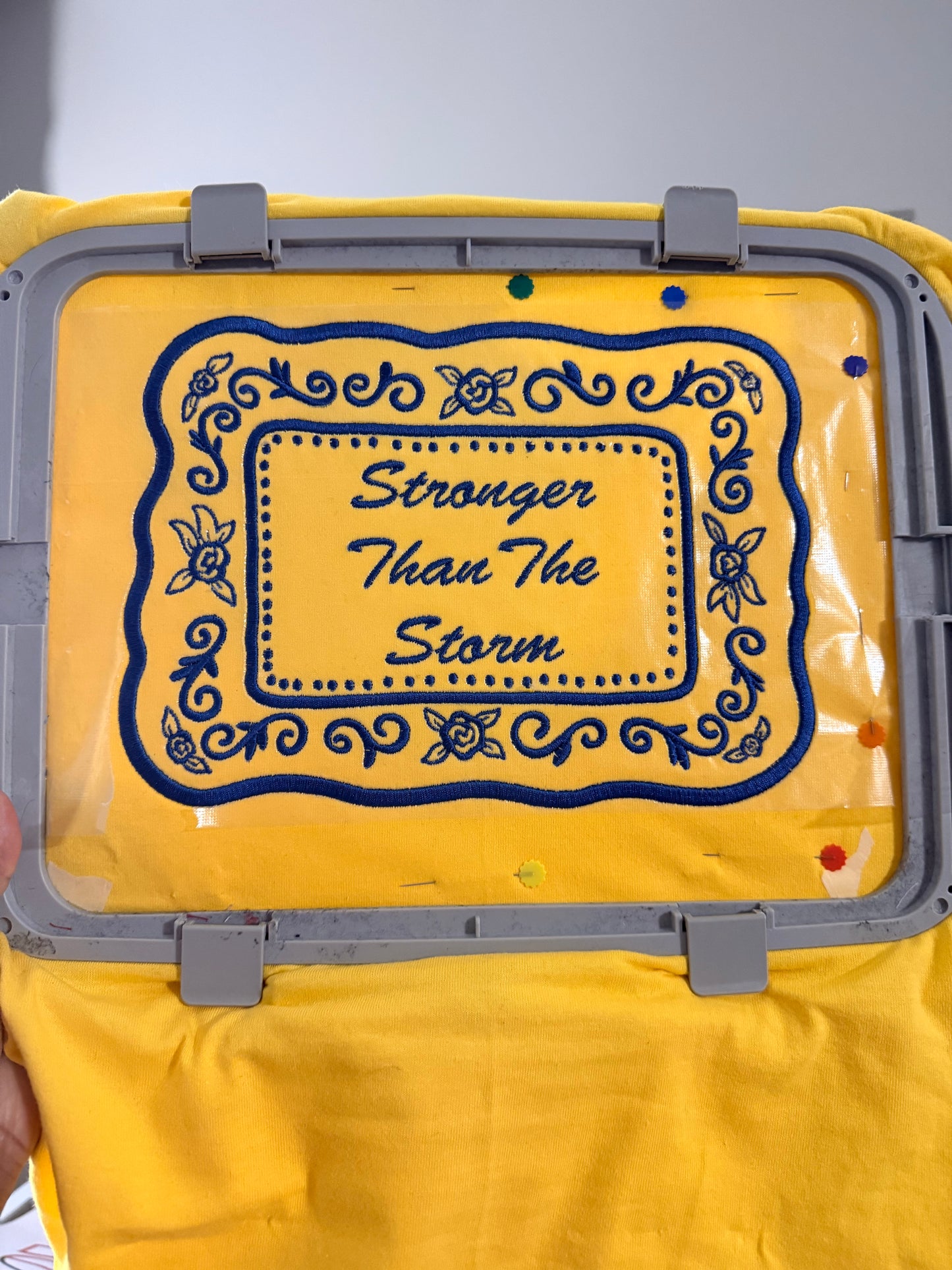 Yellow jumper with embroidery text and design on a gray embroidery hoop