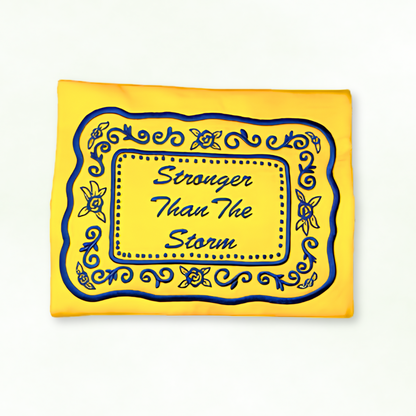 Yellow sweatshirt with blue decorative border and text 'Stronger Than The Storm' on a white background