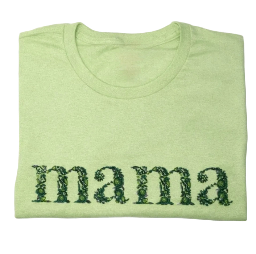 Folded green t-shirt with floral embroidery 'mama' text on a white background