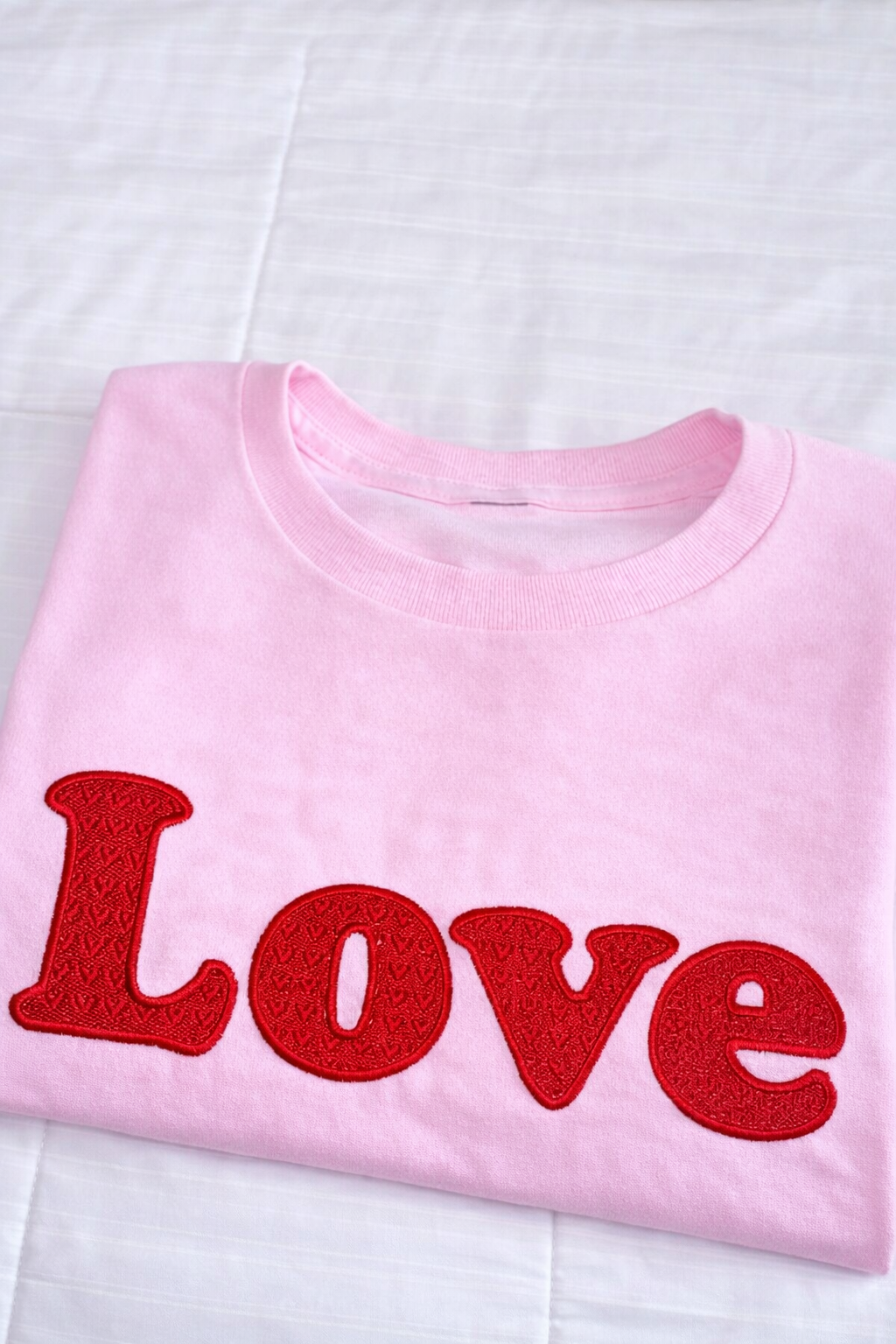 Folded pink Valentine sweatshirt featuring fully stitched LOVE embroidery on a white background