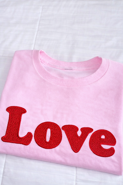 Folded pink Valentine sweatshirt featuring fully stitched LOVE embroidery on a white background