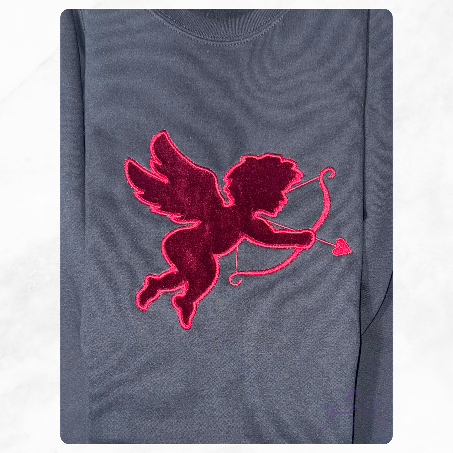 black sweatshirt with a red embroidered design of a winged figure holding an arrow and heart on a white background.