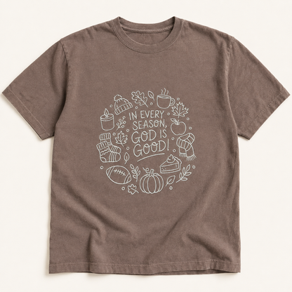 A brown short-sleeve crewneck t-shirt with a cream embroidery on the chest containing autumn-themed icons and the text 'IN EVERY SEASON, GOD IS GOOD'.
