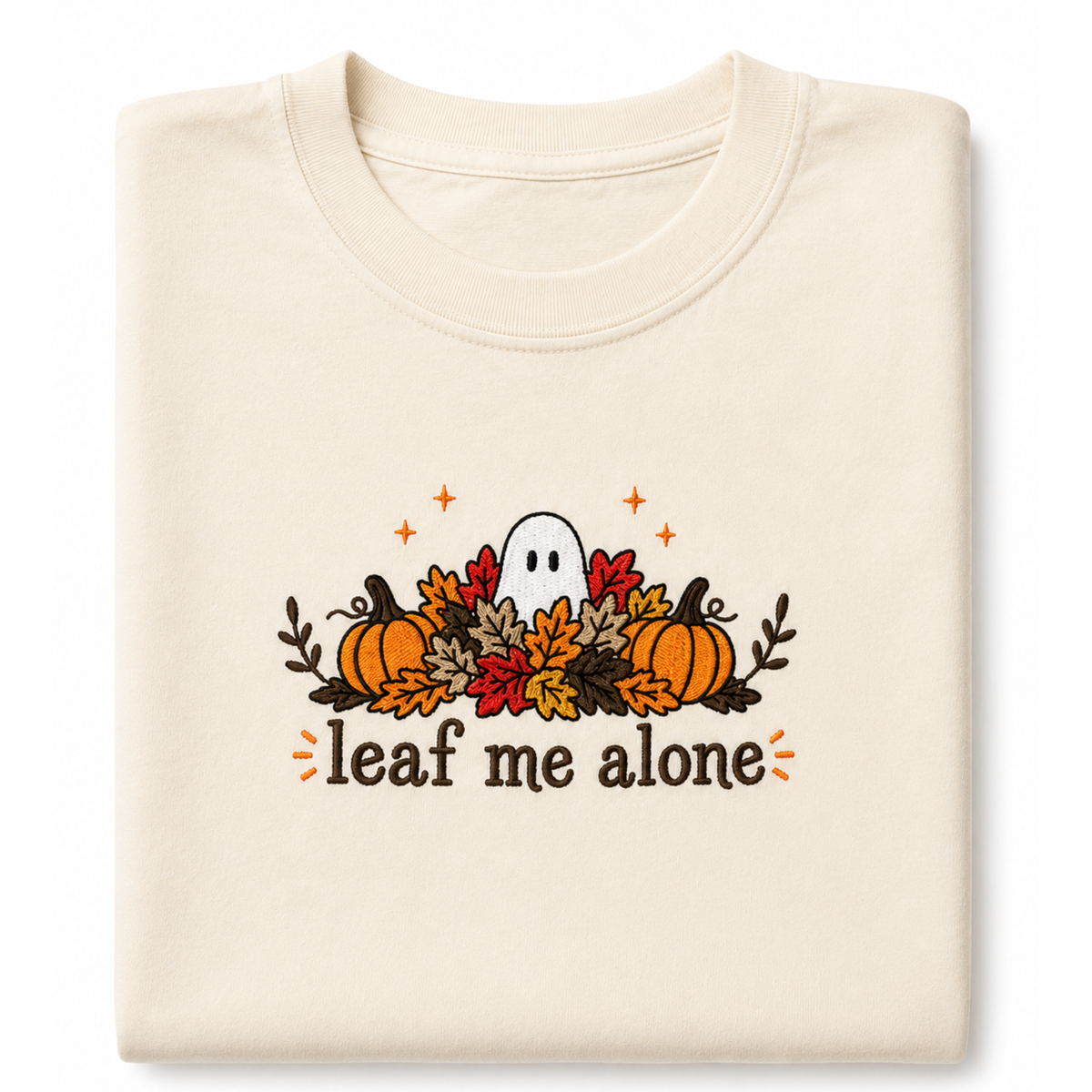 A folded cream-colored crewneck featuring a Halloween graphic with pumpkins, autumn leaves, a ghost, and the text 'leaf me alone' in brown, orange, and red.