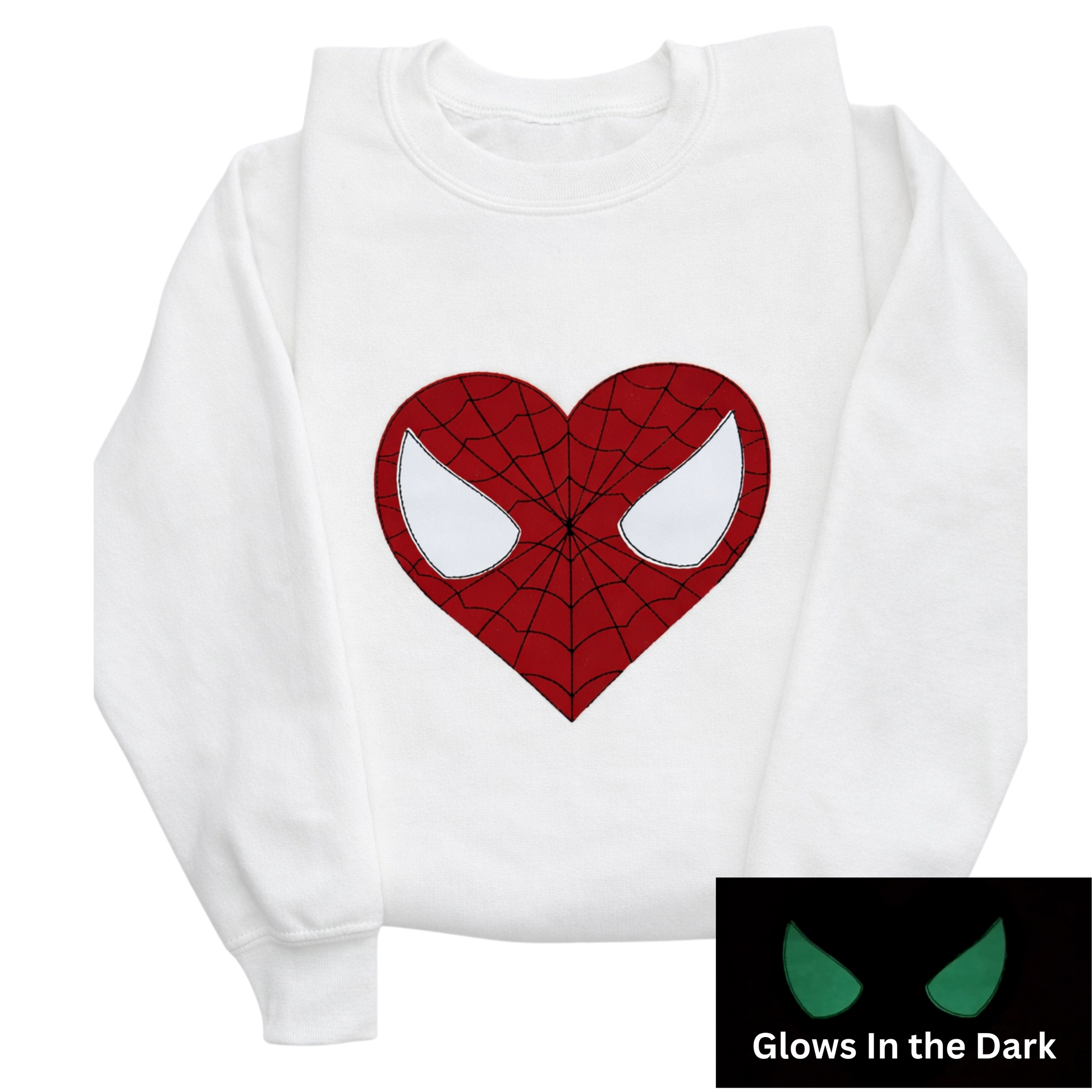 A white long-sleeve sweatshirt featuring a red spider web-heart and glow in the dark mask eyes. A small inset in the bottom right corner shows the graphic glowing green in the dark.