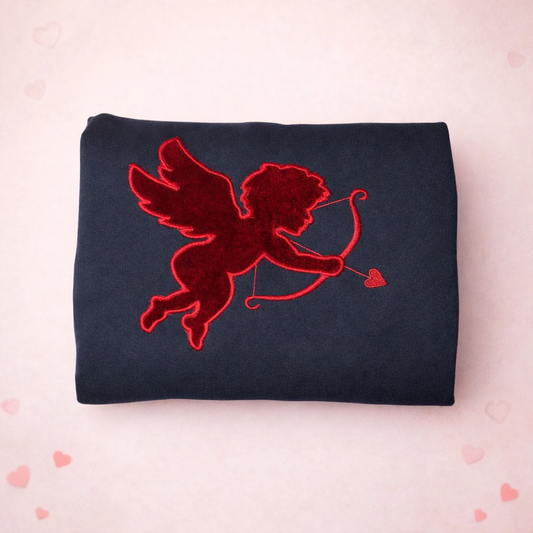 Black fabric with red velvet embroidered design of a cupid a light pink background.